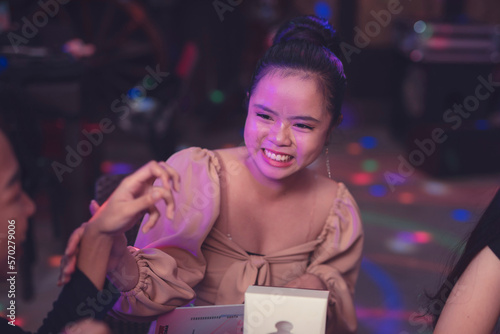 A candid photo of a happy and smiling Asian woman wearing puffed sleeved dress and a neat hair bun.