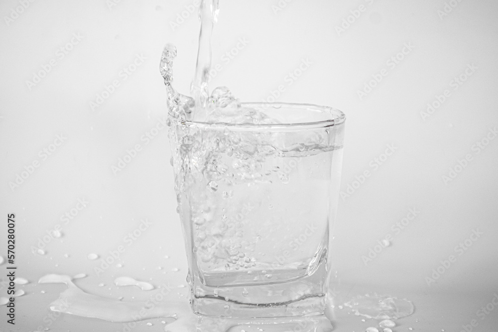 Pouring water into a glass causes splashes and water droplets on the floor.