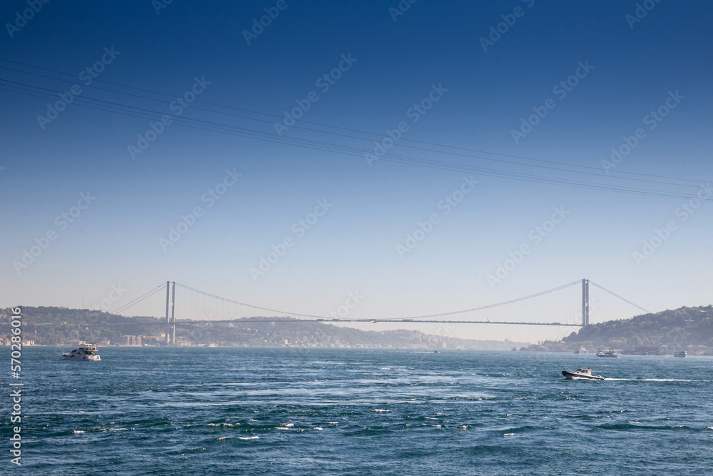 Bosphorus Bridge; also called 15 july martyrs bridge or 15 temmuz sehitler koprusu, seen from afar with boats passing on posporus strait. it's a bridge connecting Asian and European side. . Bosphorus Bridge; also called 15 july martyrs bridge or 15 temmuz sehitler koprusu, seen from afar with boats passing on posporus strait. it's a bridge connecting Asian and European side. .