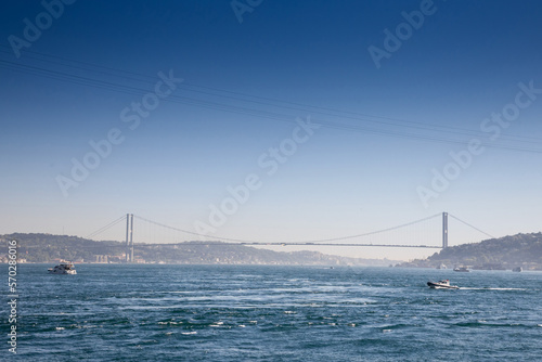 Bosphorus Bridge; also called 15 july martyrs bridge or 15 temmuz sehitler koprusu, seen from afar with boats passing on posporus strait. it's a bridge connecting Asian and European side. .