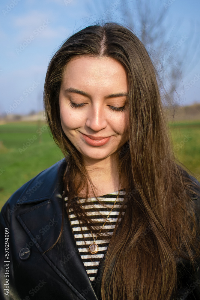 Portrait of a beautiful girl with long hair.Lonely woman walks.Emotion of joy and happiness.The girl's skin shines in the sun.The girl looks down.Nice smile.Good skin texture.No retouching.Portrait.