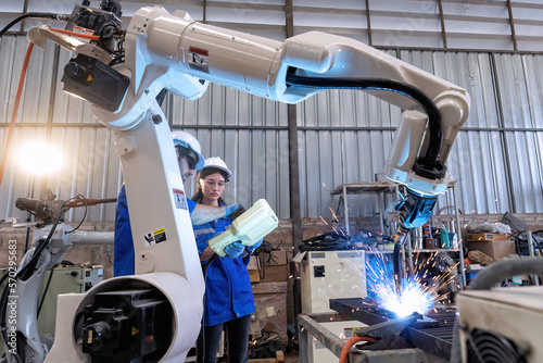 In robotic maintenance shop an engineer hold controller operate robot arm welding fire spark