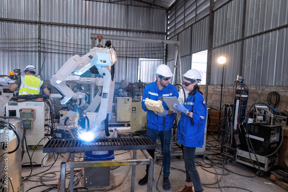 In robotic maintenance shop an engineer hold controller operate robot arm welding fire spark In robotic maintenance shop an engineer hold controller operate robot arm welding fire spark