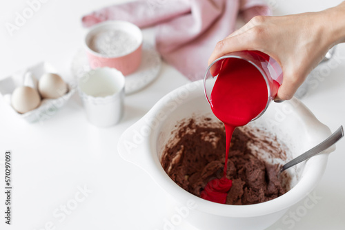 person making red velvet cake and adding red food coloring to batter. kitchen table with ingredients. cooking class concept. copy space