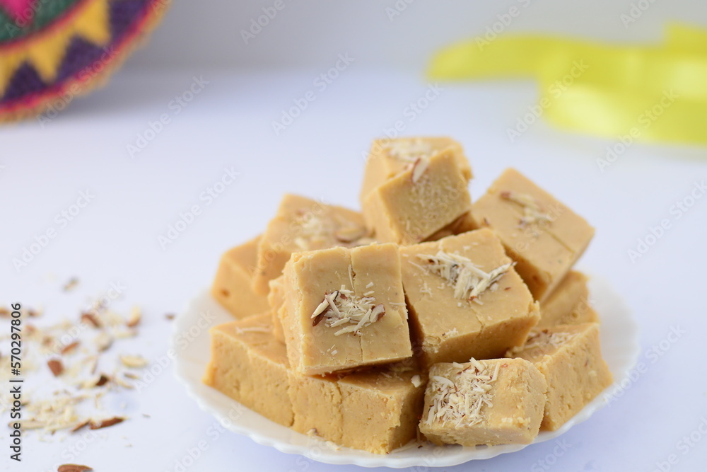 Almond barfi in bowl with some almonds on the background.