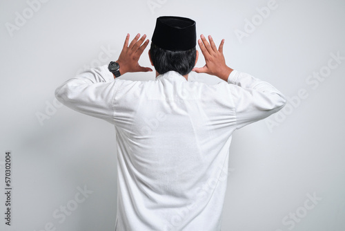 Young asian muslim man raising hand and praying standing backward