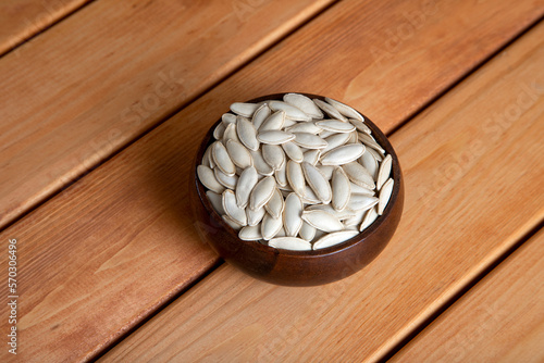 A bowl full of pumpkin seeds on wooden table,top view