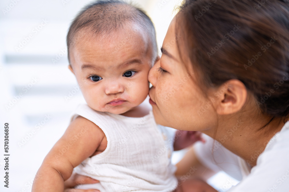 Mom happy joyful teasing asian infant baby new born sitting on bed and kiss her Mom happy joyful teasing asian infant baby new born sitting on bed and kiss her