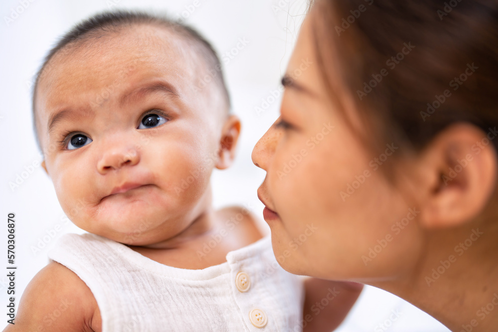 Mom happy joyful teasing asian infant baby new born sitting on bed and kiss her Mom happy joyful teasing asian infant baby new born sitting on bed and kiss her