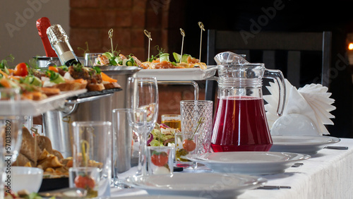 Set table with plates, wine glasses, appetisers, beverage and a buckets of champagne indoor in restaurant, selective focus.