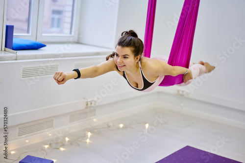 Young woman doing flying aerial yoga exercise in studio