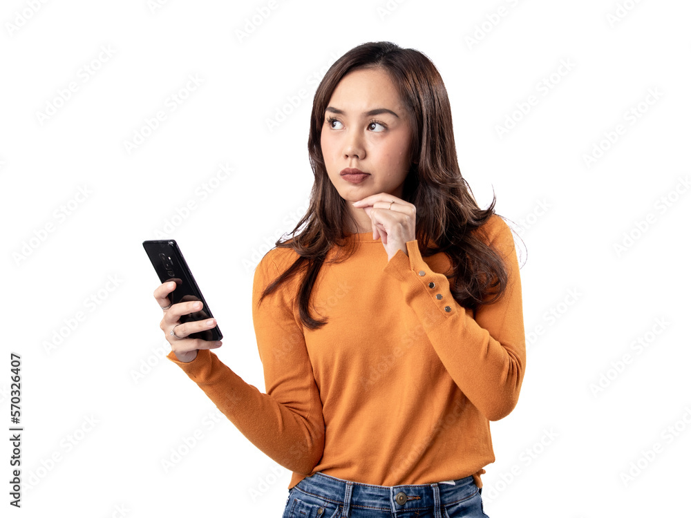 Photo features a happy Indonesian woman wearing an orange sweater and jeans while holding a smartphone, isolated on a white background. Photo features a happy Indonesian woman wearing an orange sweater and jeans while holding a smartphone, isolated on a white background.