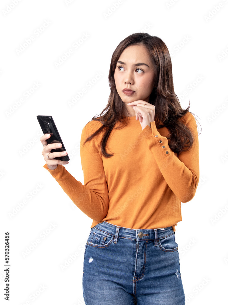 Photo features a happy Indonesian woman wearing an orange sweater and jeans while holding a smartphone, isolated on a white background.