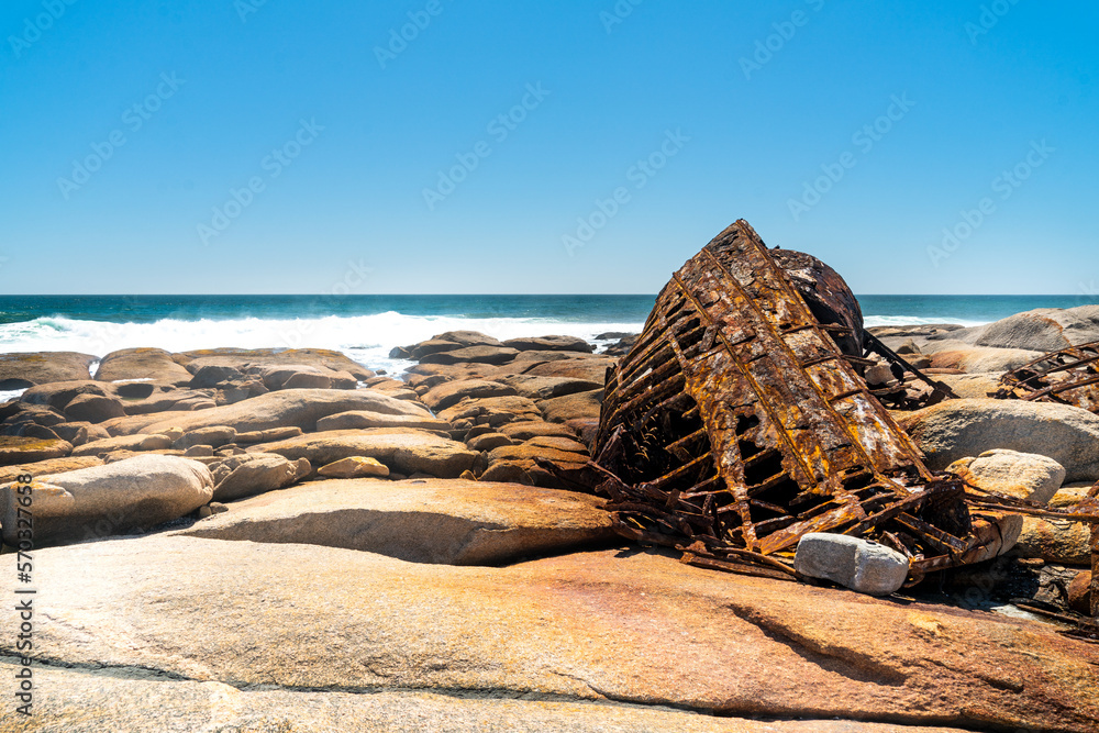 A rusty ship wreck lies on the rocks at the Atlantic Ocean Coast in South Africa.