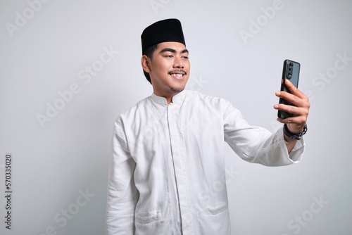 Cheerful young Asian Muslim man doing video call or selfie shot on mobile phone © Reza