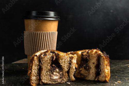 roll de canela partido por la mitad para ver su interior corte vertical con taza de cafe delivery para mostrar el tamaño  photo