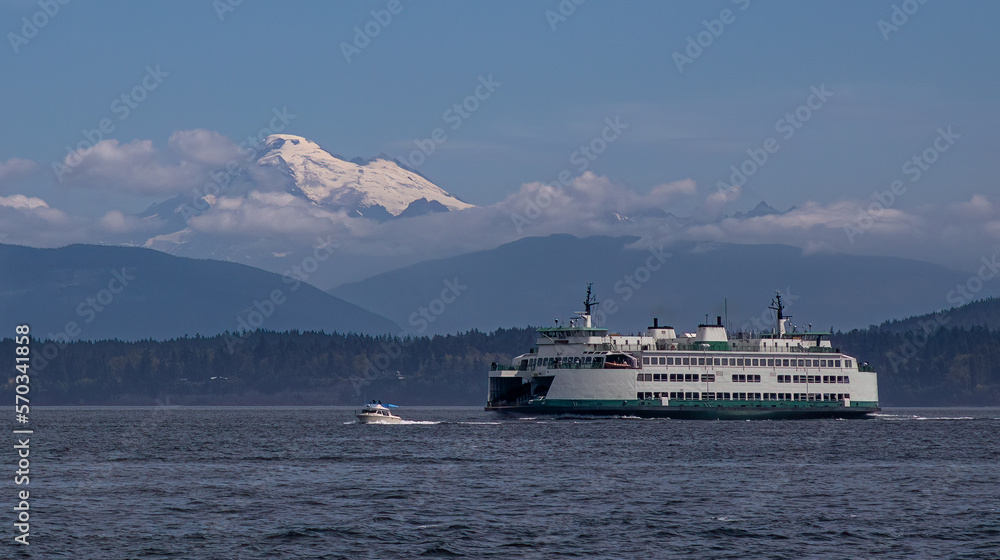A small powerboat and a Washington State Ferry transit the San Juan Islands near Anacortes, Washington with a stately Mount Baker towering in the background.