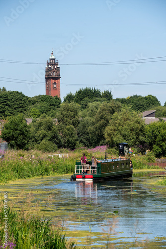 Tableau sur toile Narrow Boat sailing along Forth & Clyde Canal in Glagow with derelict tower of former hospital in background