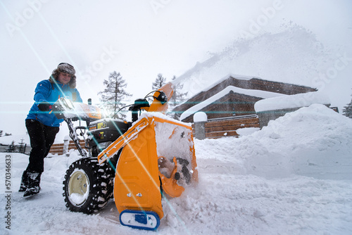 Removing snow from the area using a yellow snow-covered snowblower. Clearing the access road to the house from snowfall.