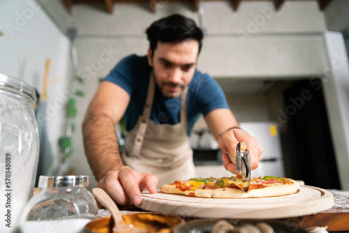 handsome chef cut delicious homemade italian mozzarella pizza after prepare and bake from stove or oven for lunch meal or dinner in local italian pizza restaurant