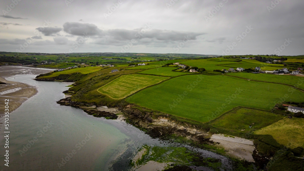 Obraz premium Green fields on the Irish hills, top view. The countryside of Ireland on a cloudy day. The coast of Clonakilty Bay at low tide. Green grass field under cloudy sky