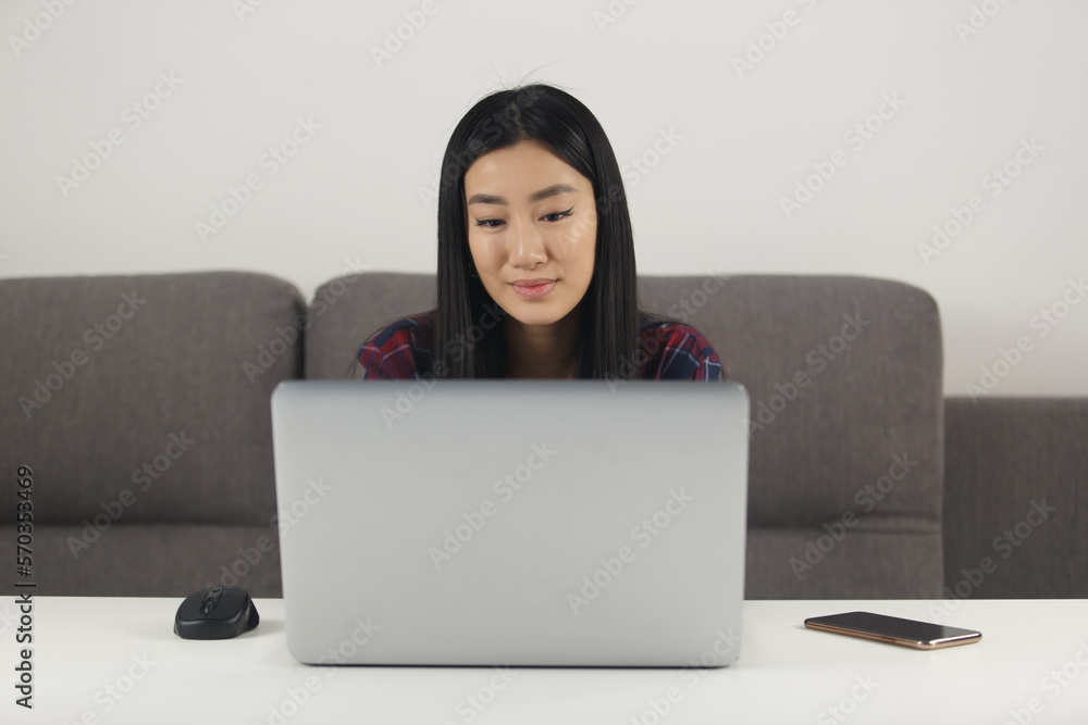 Young Asian girl studying online. Portrait of Vietnamese POC female working on modern silver laptop computer at home