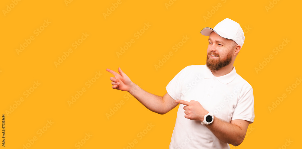 Banner size shot of a bearded man wearing white T shirt and cap pointing aside over yellow background.