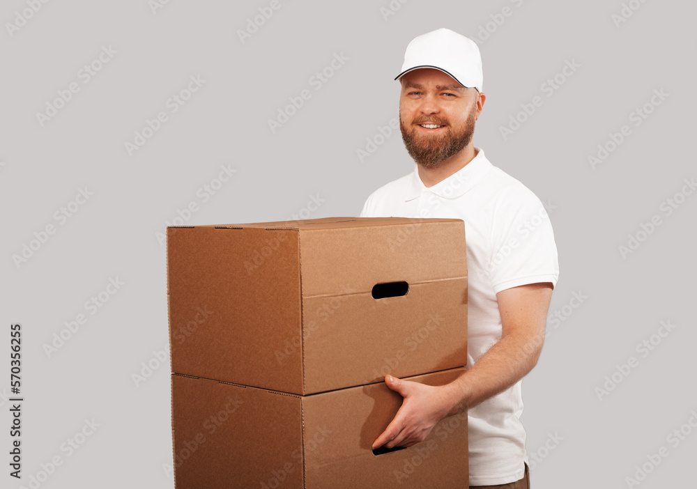 Smiling delivery man wearing white uniform hold some big moving boxes. Studio shot over grey background. Smiling delivery man wearing white uniform hold some big moving boxes. Studio shot over grey background.