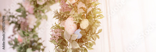 happy easter and spring holidays time. easter wreath with sprigs of lilac bush blossom flowers and leaves and decorated eggs on bright light window background. home interior decor. banner. flare