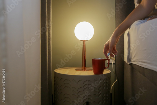 Картината върху платно Woman in bed reaching for her first morning coffee from the nightstand