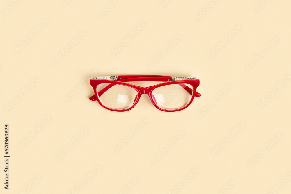 Red female glasses with transparent lenses on neutral beige color pastel background. Top view copy space. Minimal design. Woman's eyeglasses. Trendy modern minimalistic flat lay. One Eyewear. Close up