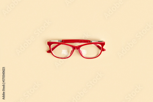 Red female glasses with transparent lenses on neutral beige color pastel background. Top view copy space. Minimal design. Woman's eyeglasses. Trendy modern minimalistic flat lay. One Eyewear. Close up