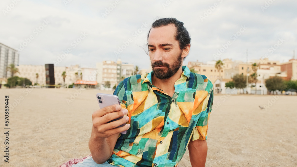 Young man sitting and using mobile phone on the beach