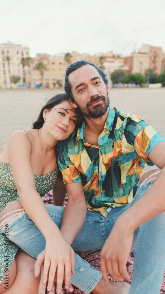 Obraz premium Happy couple sitting hugging on blanket on the beach