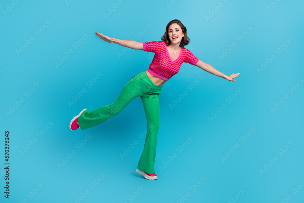 Full length photo of pleasant nice cute girl with curly hairdo dressed pink top green pants flying isolated on blue color background