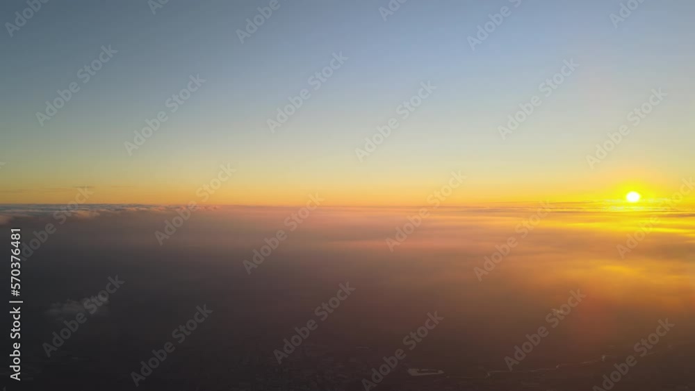 View from high altitude of bright colorful sunset sky with vivid smooth layer of clouds illuminated with setting sun light spreading to horizon View from high altitude of bright colorful sunset sky with vivid smooth layer of clouds illuminated with setting sun light spreading to horizon