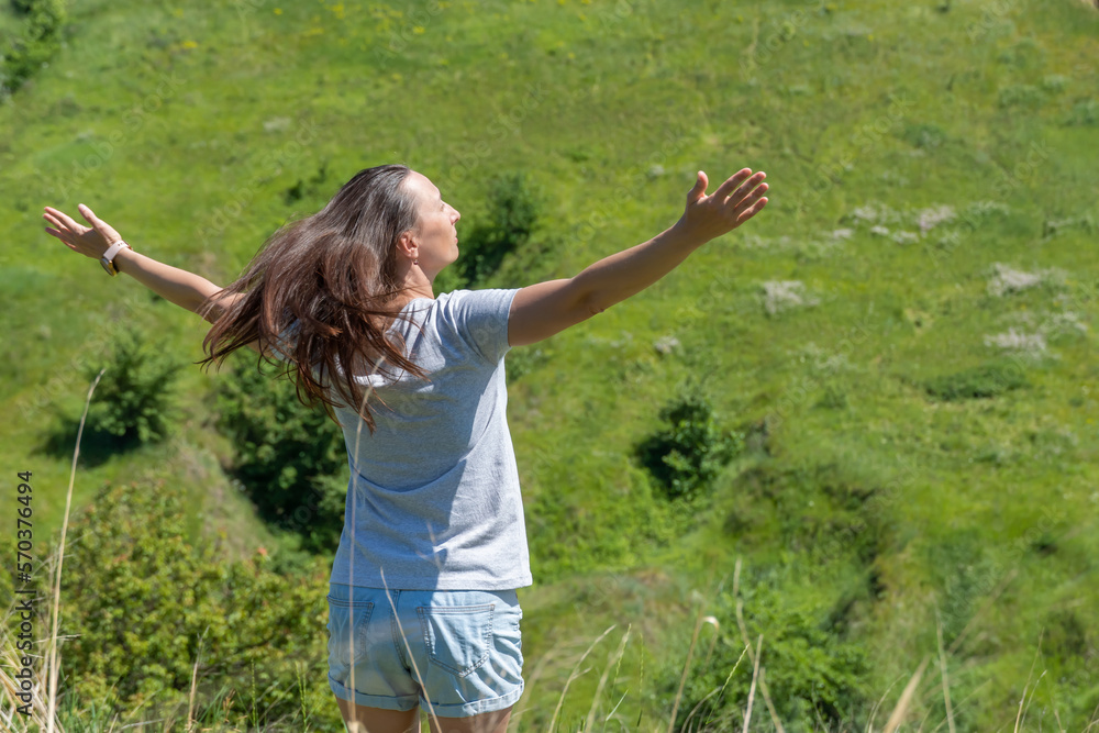 Happy woman greeting sun in ravine covered with greenery. Young female raise hands to the sunshine. She looking on valley and showing freedom gesture. Positive joyful of emotion surya namaskar. Happy woman greeting sun in ravine covered with greenery. Young female raise hands to the sunshine. She looking on valley and showing freedom gesture. Positive joyful of emotion surya namaskar.