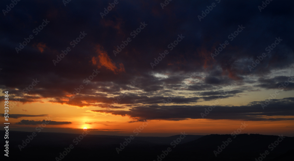 Fiery sunset view from Colley Hill between Reigate and Dorking in Surrey, UK. Surrey Hills area of Outstanding Natural Beauty on the North Downs. Dark clouds, silhouette landscape and orange sky.