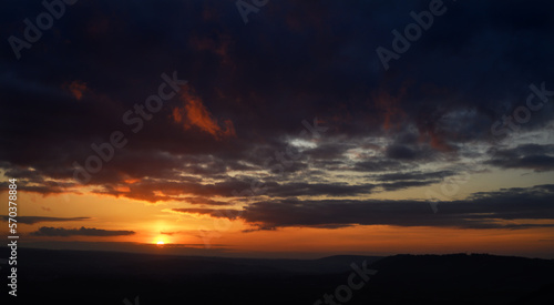 Fiery sunset view from Colley Hill between Reigate and Dorking in Surrey, UK. Surrey Hills area of Outstanding Natural Beauty on the North Downs. Dark clouds, silhouette landscape and orange sky.