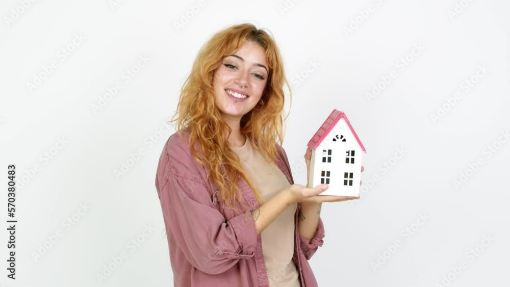 Young redhead woman holding a little house over isolated background Young redhead woman holding a little house over isolated background