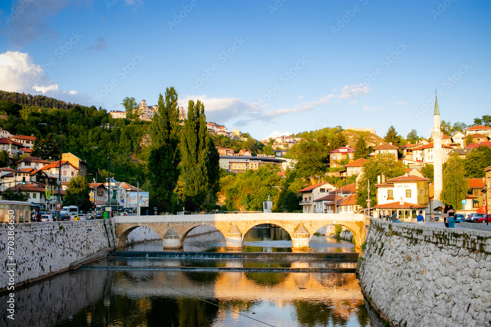 Paisaje de la ciudad de Sarajevo, Puente romano atravesando un río  con casas de fondo
