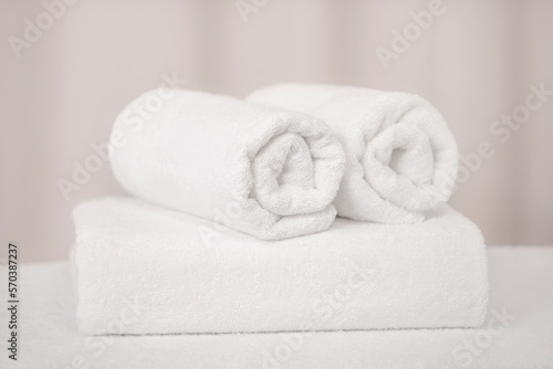 Three white terry bath towels are twisted on a light background