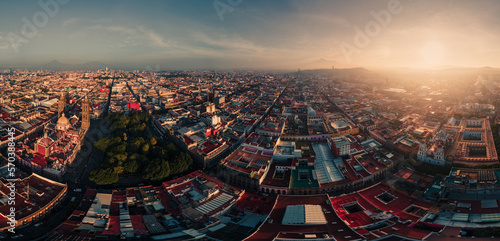 Panorama aéreo de un amanecer con el zócalo en primer plano y el resto de la ciudad y los volcanes de fondo