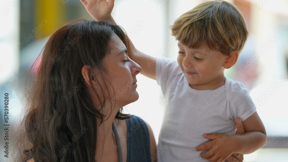Cute lifestyle moment of mother and child hanging out together in sunny day outside. Little boy tapping mother head candid and authentic Cute lifestyle moment of mother and child hanging out together in sunny day outside. Little boy tapping mother head candid and authentic
