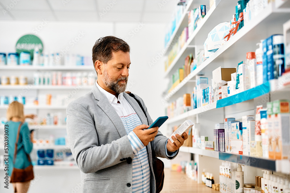 Middle aged man using mobile phone while buying medicine in drugstore.