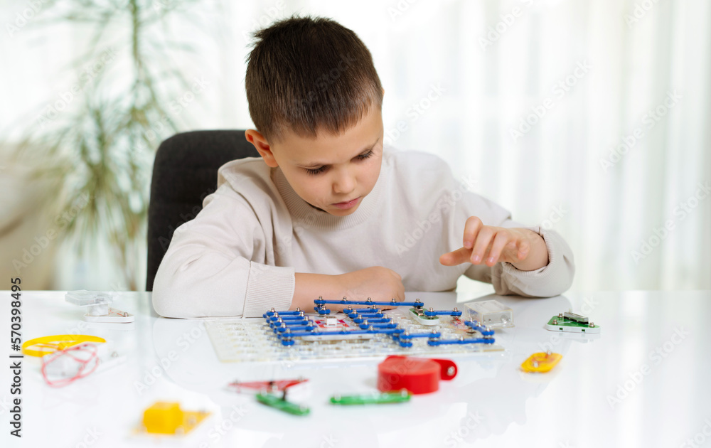 Child boy plays with an electronic constructor at home at the table. Future engineer learns to assemble electronic circuits. Creative hobby Child boy plays with an electronic constructor at home at the table. Future engineer learns to assemble electronic circuits. Creative hobby
