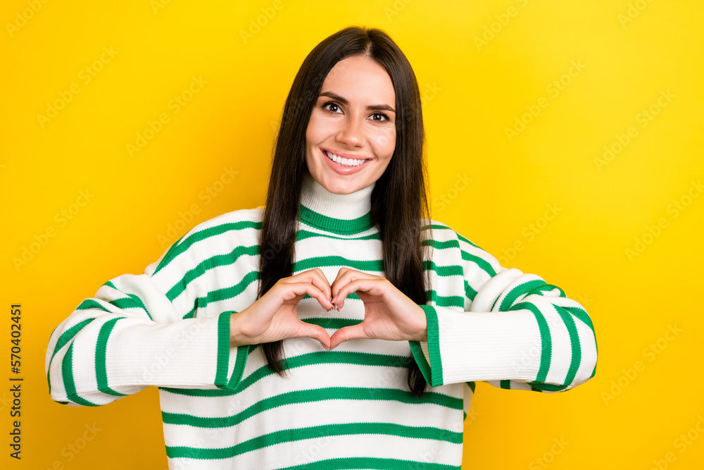 Photo of positive adorable lady dressed striped pullover smiling showing arms heart isolated yellow color background Photo of positive adorable lady dressed striped pullover smiling showing arms heart isolated yellow color background