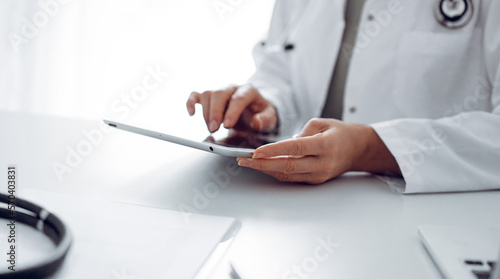 Unknown doctor woman sitting and writing notes at the desk in clinic or hospital office, close up. Medicine concept