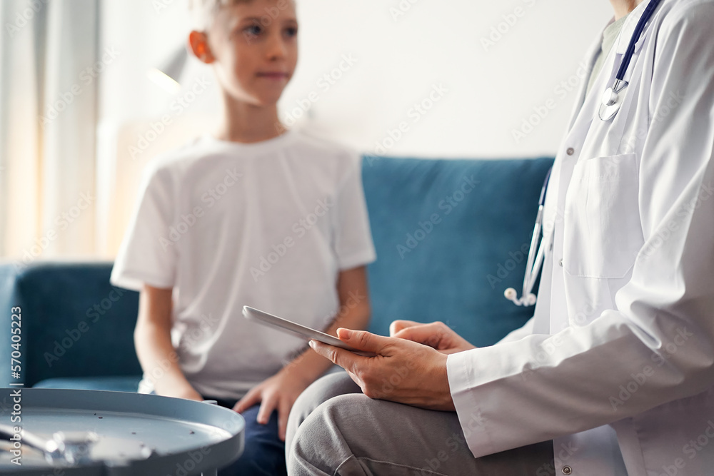 Doctor woman and kid boy patient at home. The pediatrician using tablet computer while filling up medical records, close up. Medicine, healthcare concepts Doctor woman and kid boy patient at home. The pediatrician using tablet computer while filling up medical records, close up. Medicine, healthcare concepts