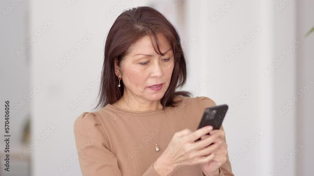 Closeup attractive stylish mature woman in brown top texting business on smartphone sitting in chair at home Closeup attractive stylish mature woman in brown top texting business on smartphone sitting in chair at home